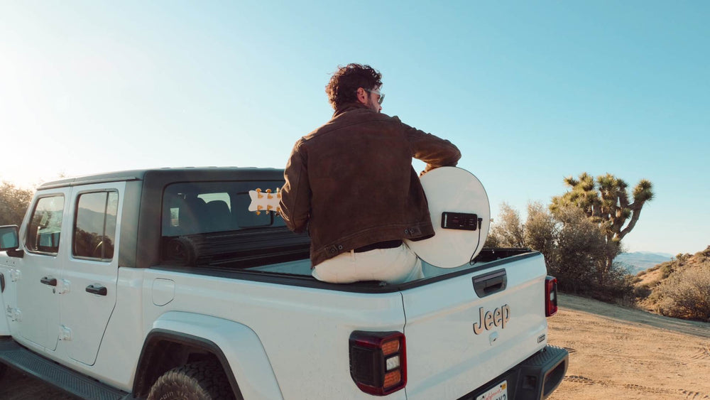 Musician sitting in a truck bed holding a round acoustic guitar with a ToneWoodAmp2 attached