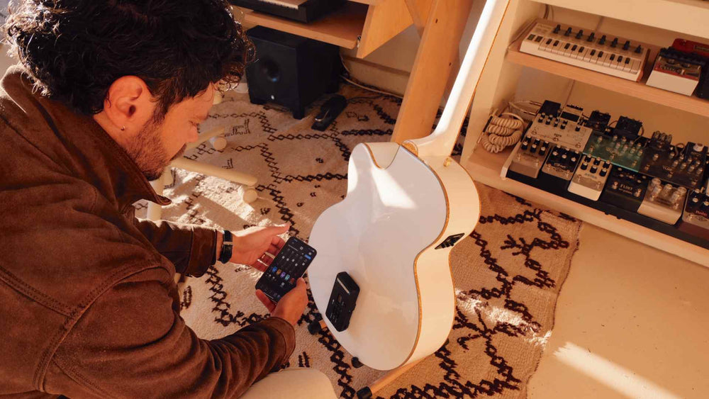 Musician adjusting the ToneWoodAmp2 app on his phone next to a white acoustic guitar